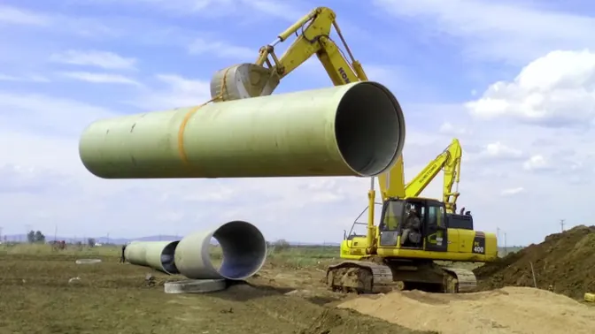 Excavators lifting a large-diameter GRP fiberglass pipe on site